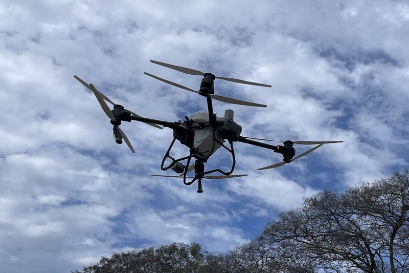 Large agricultural spray drone with its tank and spray arms in flight against a cloudy sky